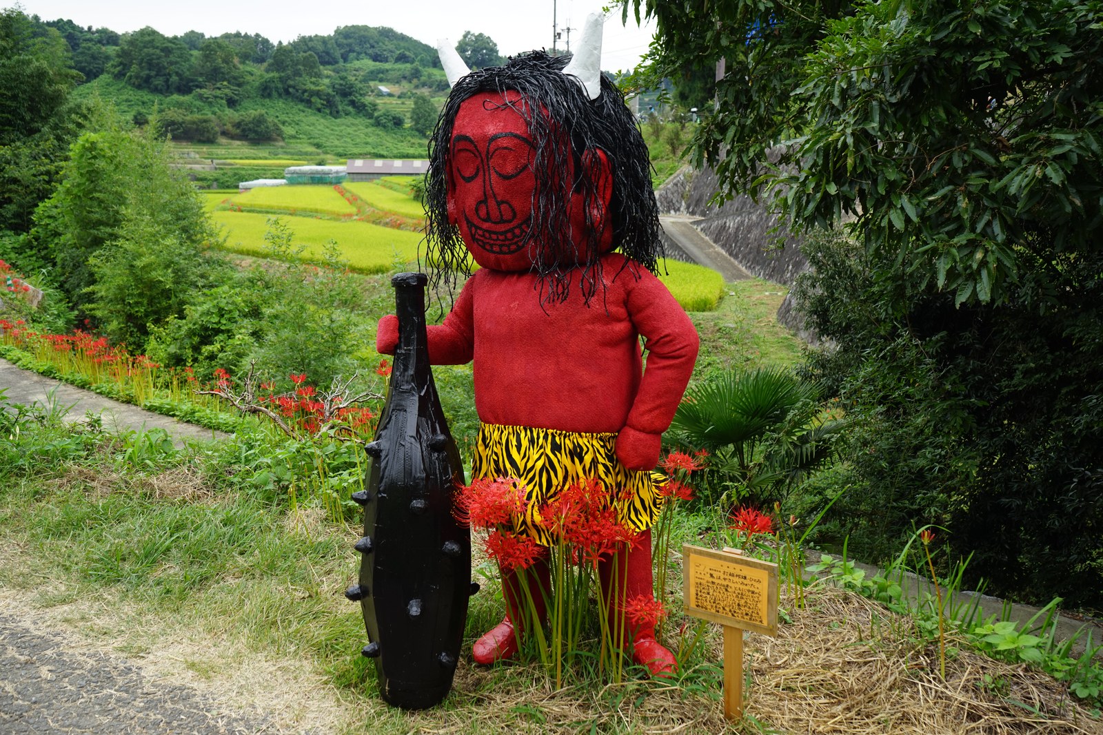 赤鬼の姿をした大きな案山子と、足元の彼岸花