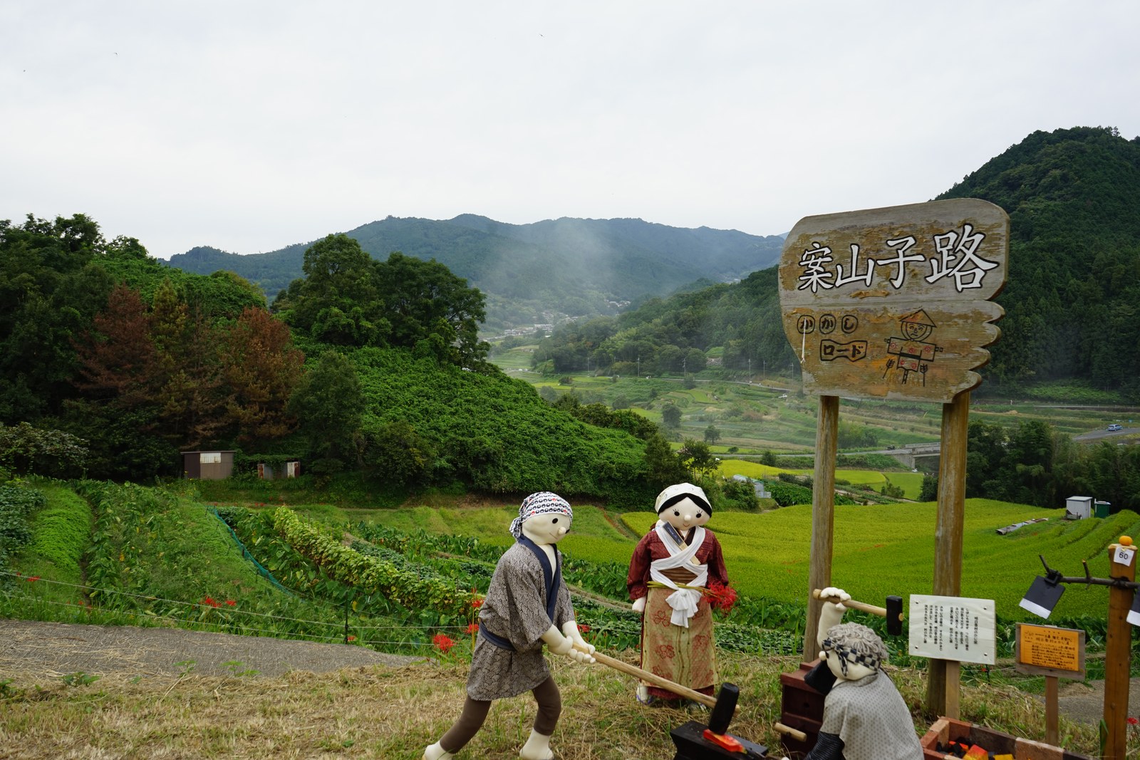 案山子路の看板と、農作業をする姿の案山子たち