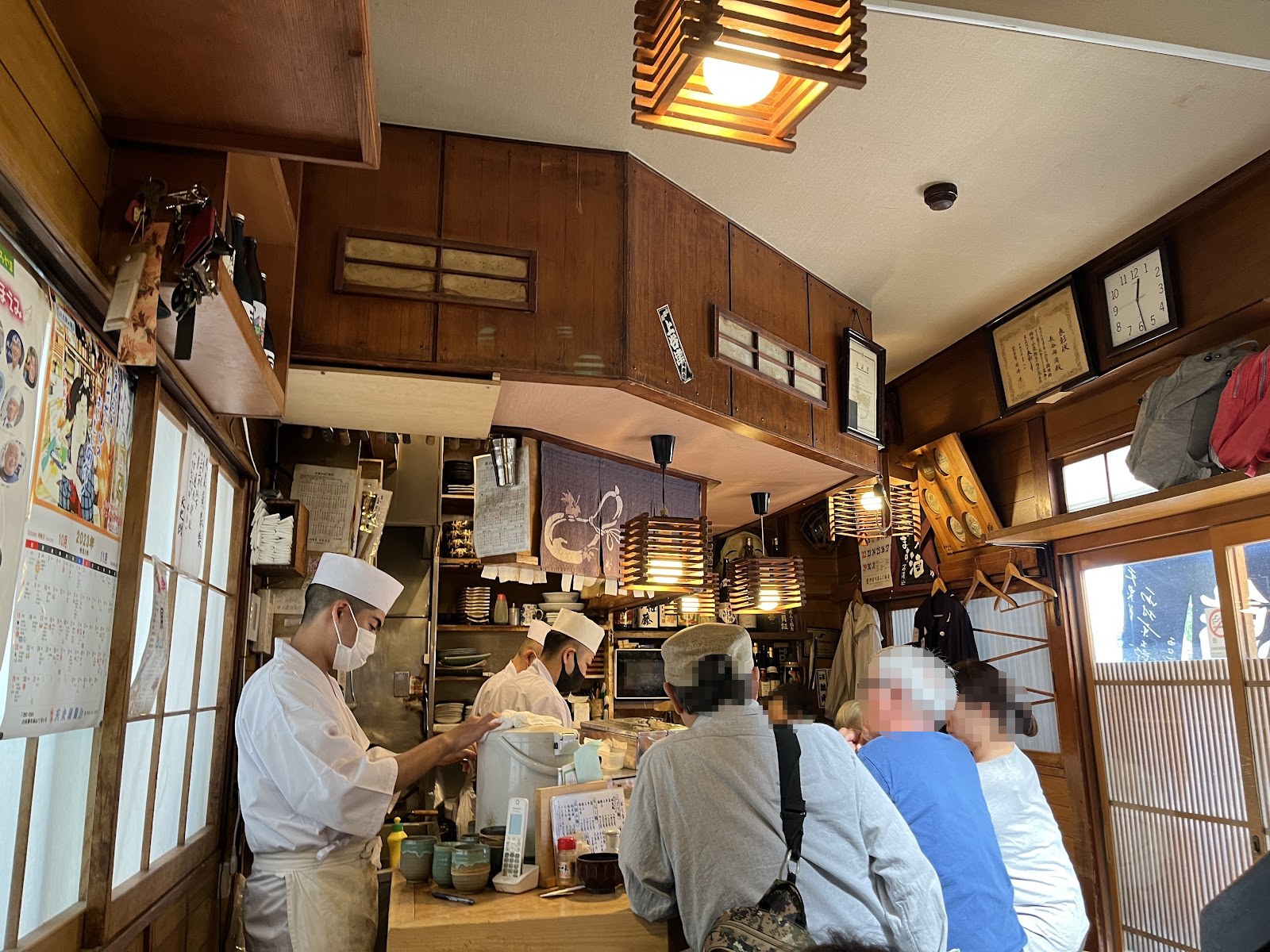 天史朗鮨の店内。カウンターに並ぶ客と、白い帽子の職人